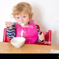 bebe-de-un-ano-de-edad-messily-comer-yogur-con-una-cuchara-inglaterra-reino-unido-f68mnd