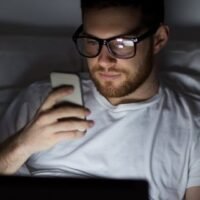 man with laptop and smartphone at night in bed