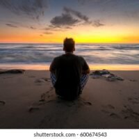 man-sitting-watching-sunset-over-260nw-600674543