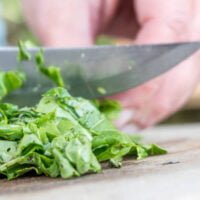 Hands Chopping Spinach Leaves On Cutting Board