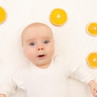 Portrait of a baby on a white background with oranges. Bedding for children. 8 months. A healthy child in body-pajamas. Citrus Allergy in children